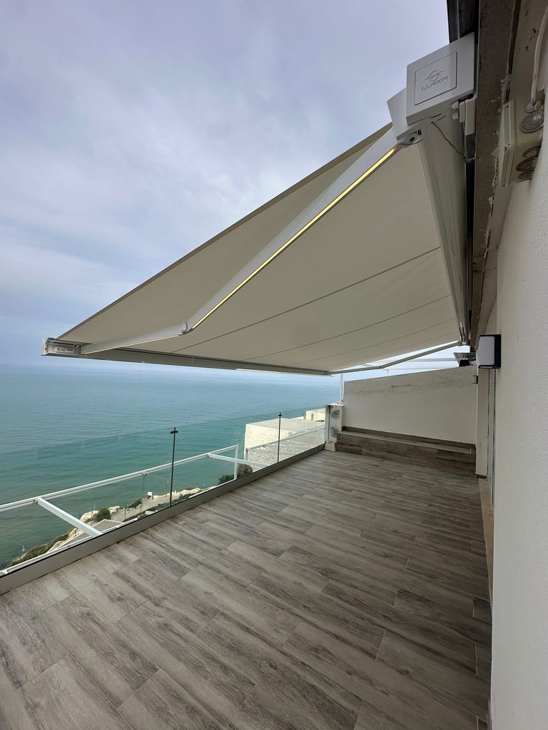 Brazo de toldo con luz LED cálida sobre una terraza frente a la playa de Cullera