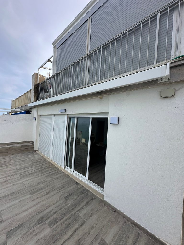 Toldo motorizado con cofre blanco sobre una terraza junto al mar